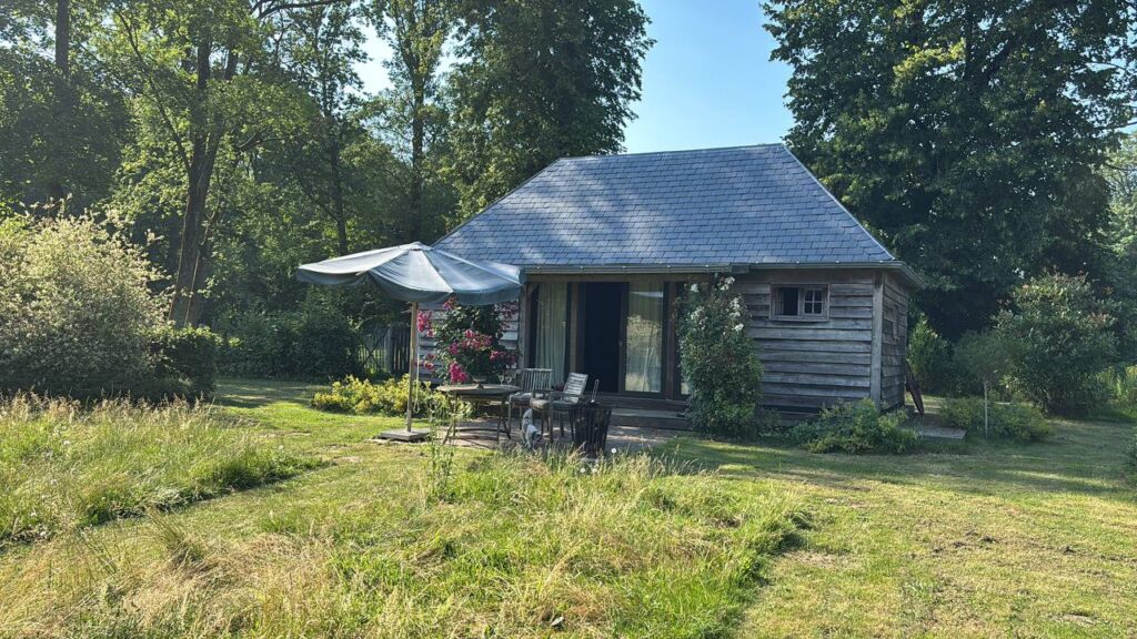 Houten hutje met leien dak in de Ardennen, terras met parasol en rozen, zomerochtend